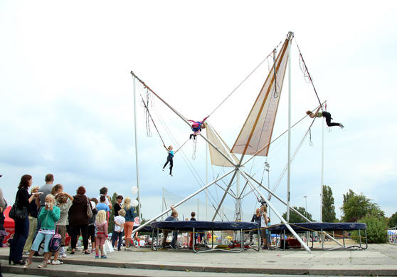 Vier Kinder springen auf einem Bungee-Trampolin und machen Kunststücke in der Luft.